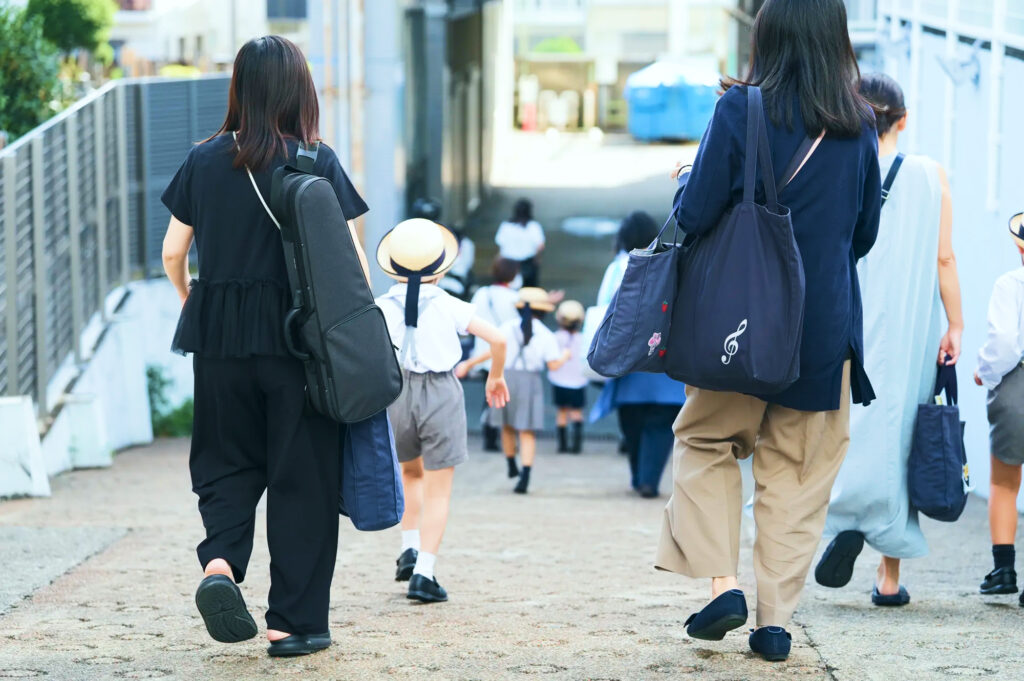 子どもと手をつないで幼稚園へ向かう保護者たち