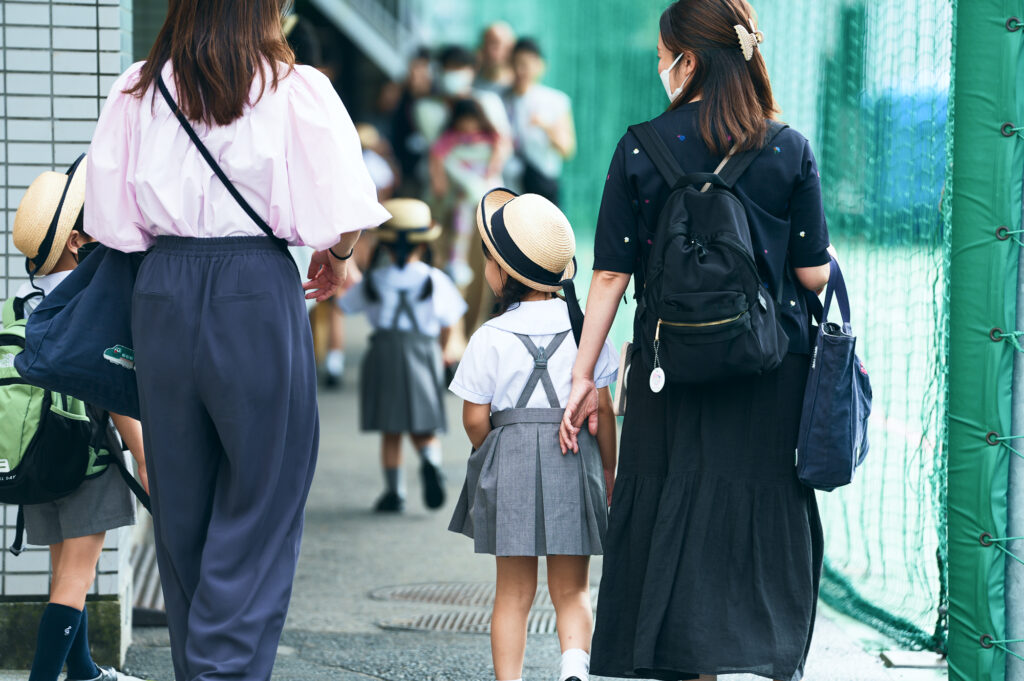 幼稚園の門の前で子どもを見送る保護者たち