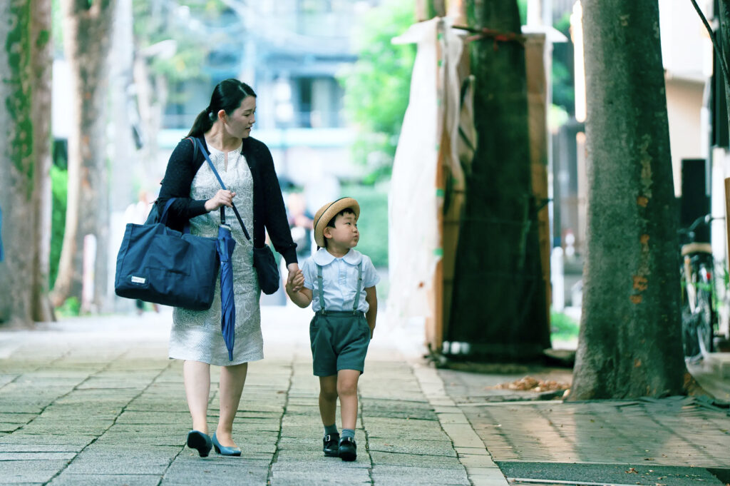 木立のある道を親子で歩く通園風景