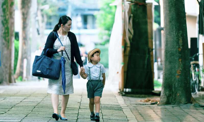 木立のある道を親子で歩く通園風景