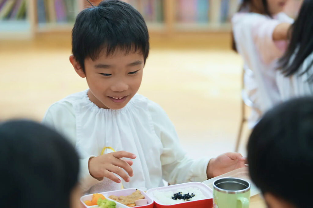 給食のお弁当を前に笑顔を見せる園児