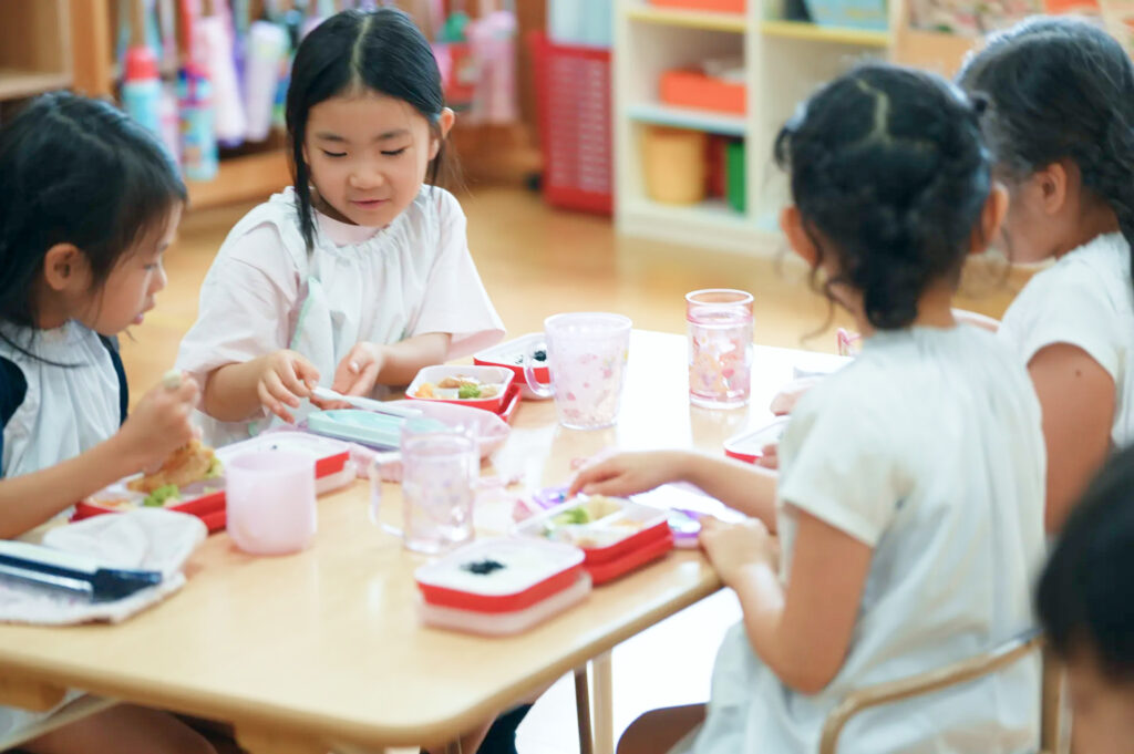 テーブルを囲み、給食のお弁当を開く子どもたち