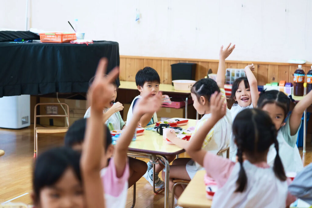 給食の時間に席で手を挙げる子どもたち