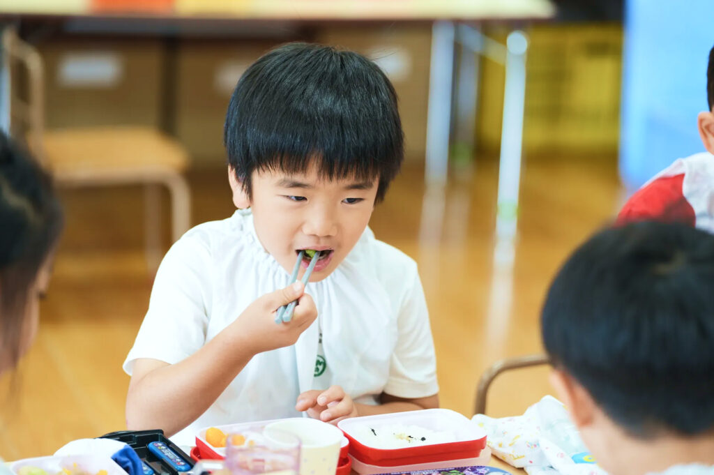 箸で給食のおかずを食べる園児